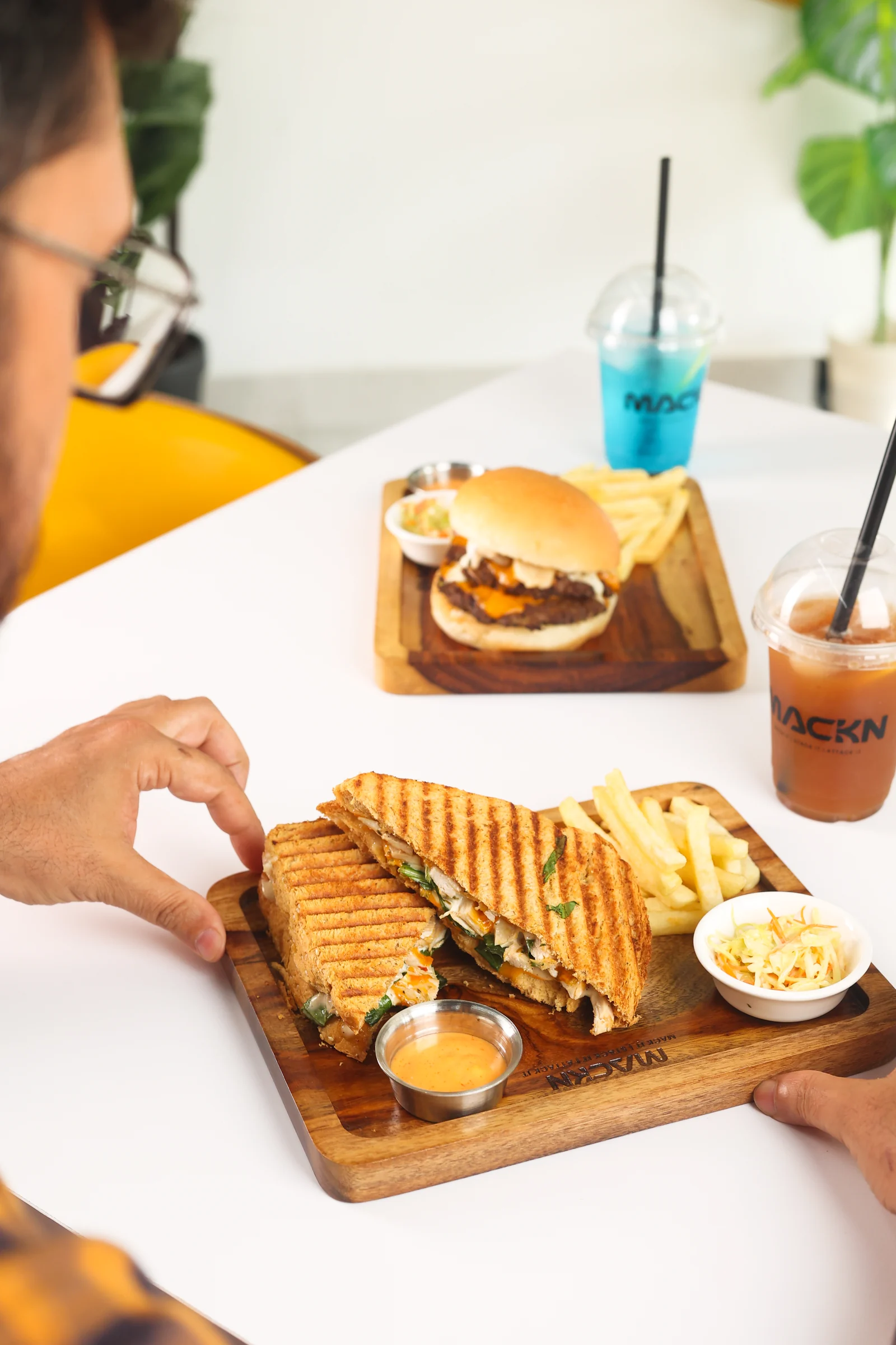 A guest reaching for a grilled sandwich at the MACKN table, with burgers and cold drinks